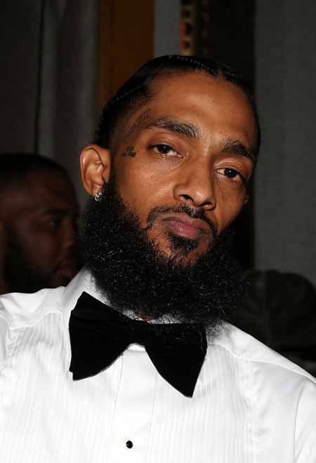 Nipsey Hussle looks at the camera wearing a black bow tie on a white shirt.